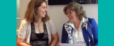 Adele Warner sits to the right on a sofa with Claudia Freeman to the left. They are talking and smiling with one another.
