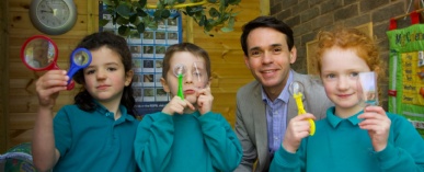 Stephen Ward smiling at the camera with a group of three Stephen Perse Cambridge Junior School students blowing bubbles.